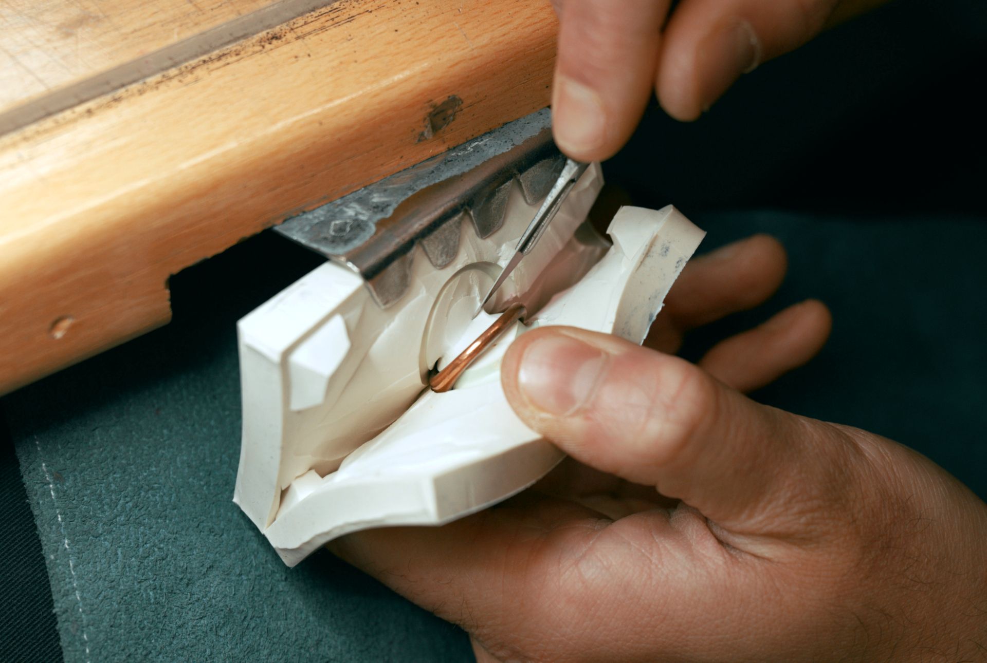 A close-up shot of a person's hands using a tool to carefully work on a piece of jewellery set in a white mould.