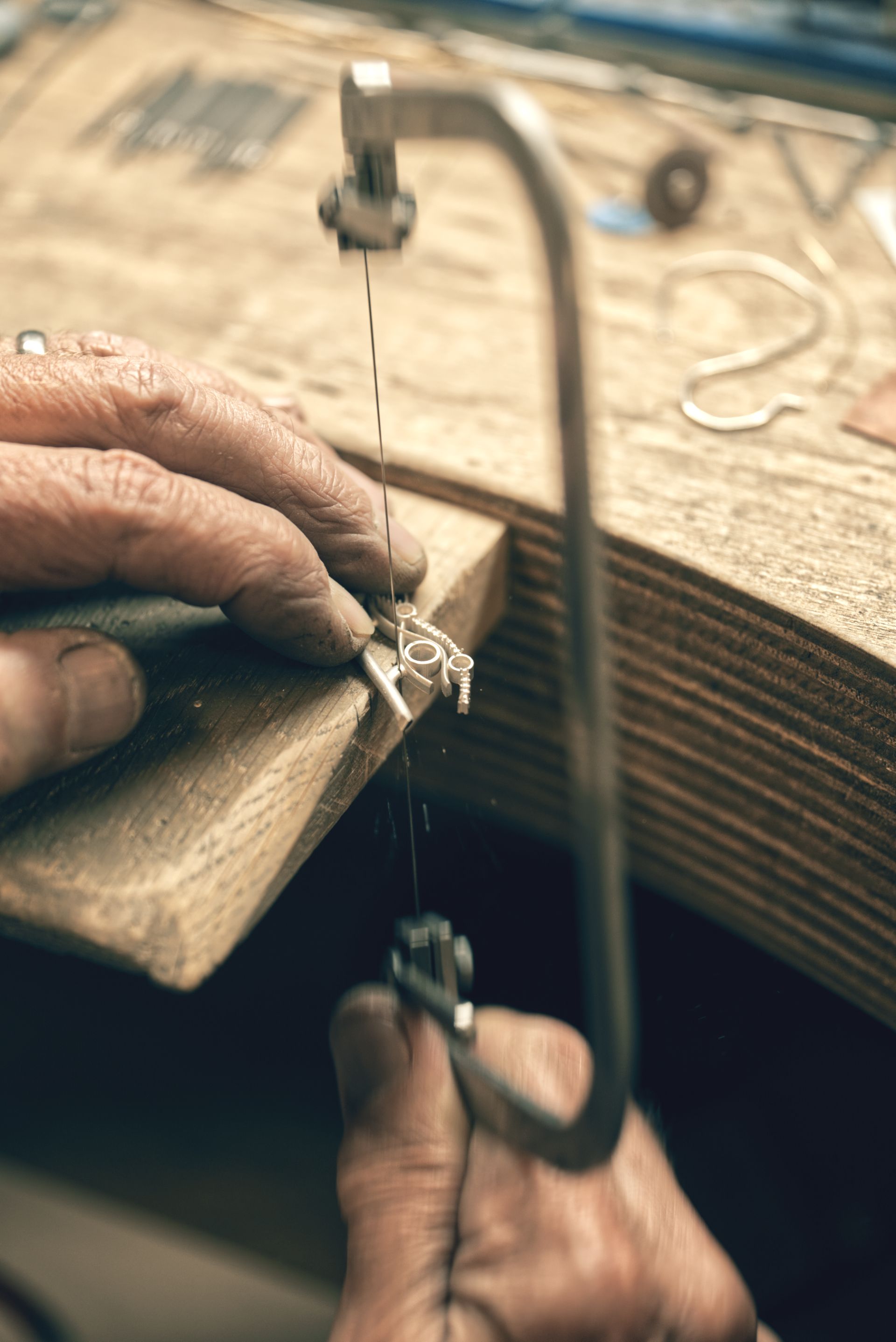 Close-up of skilled hands using a jeweler's saw to meticulously cut metal on a wooden workbench, conveying craftsmanship and focus.