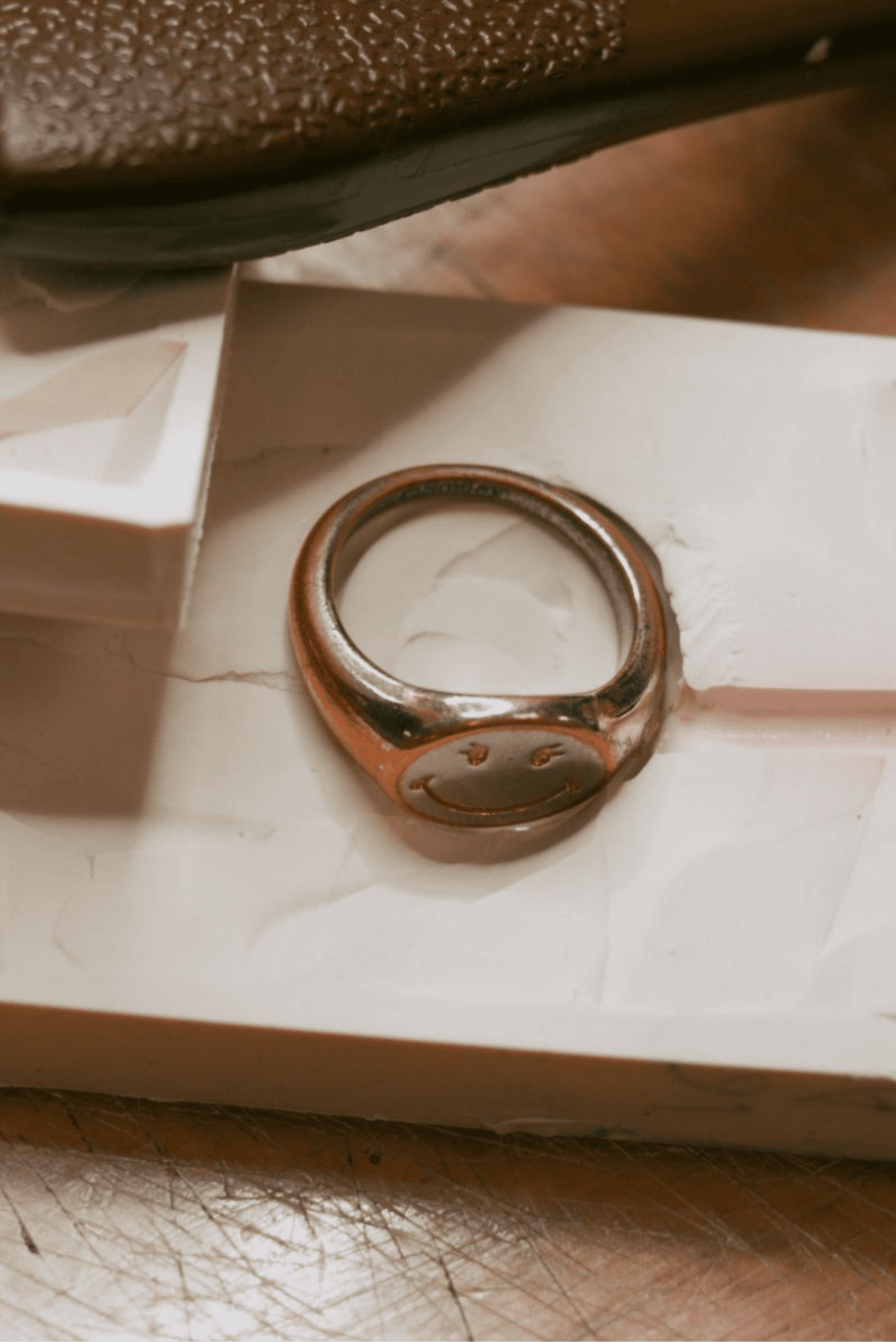 A vertical, close-up shot of a two-toned signet ring with a smiley face design, lying on a white, waxy mold