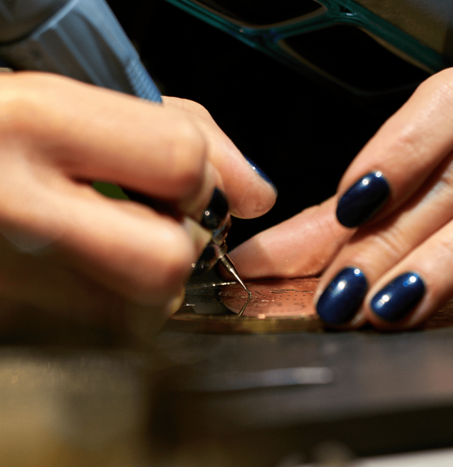 a person with blue nail polish adds the finishing touches to a piece of jewellery