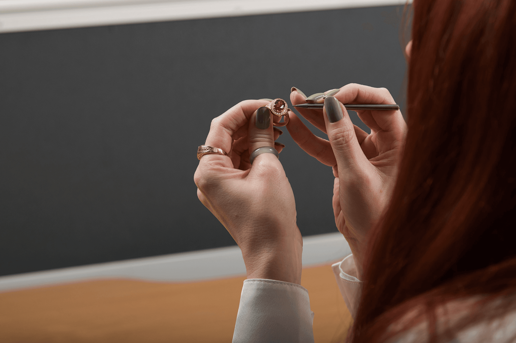 a person with red hair inspecting a piece of jewellery