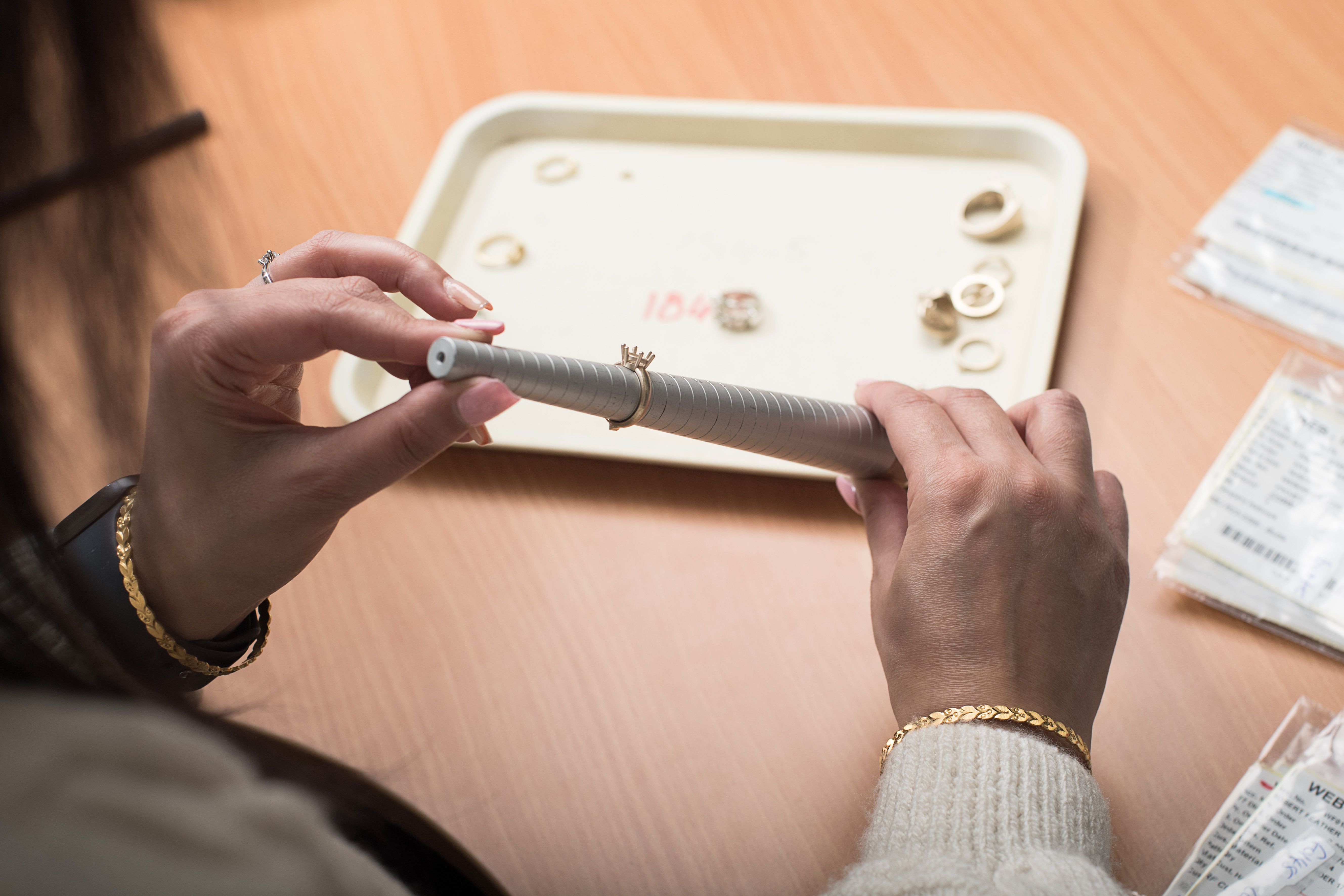 A person's hands are shown holding a ring sizer with a ring on it, presumably measuring its size.