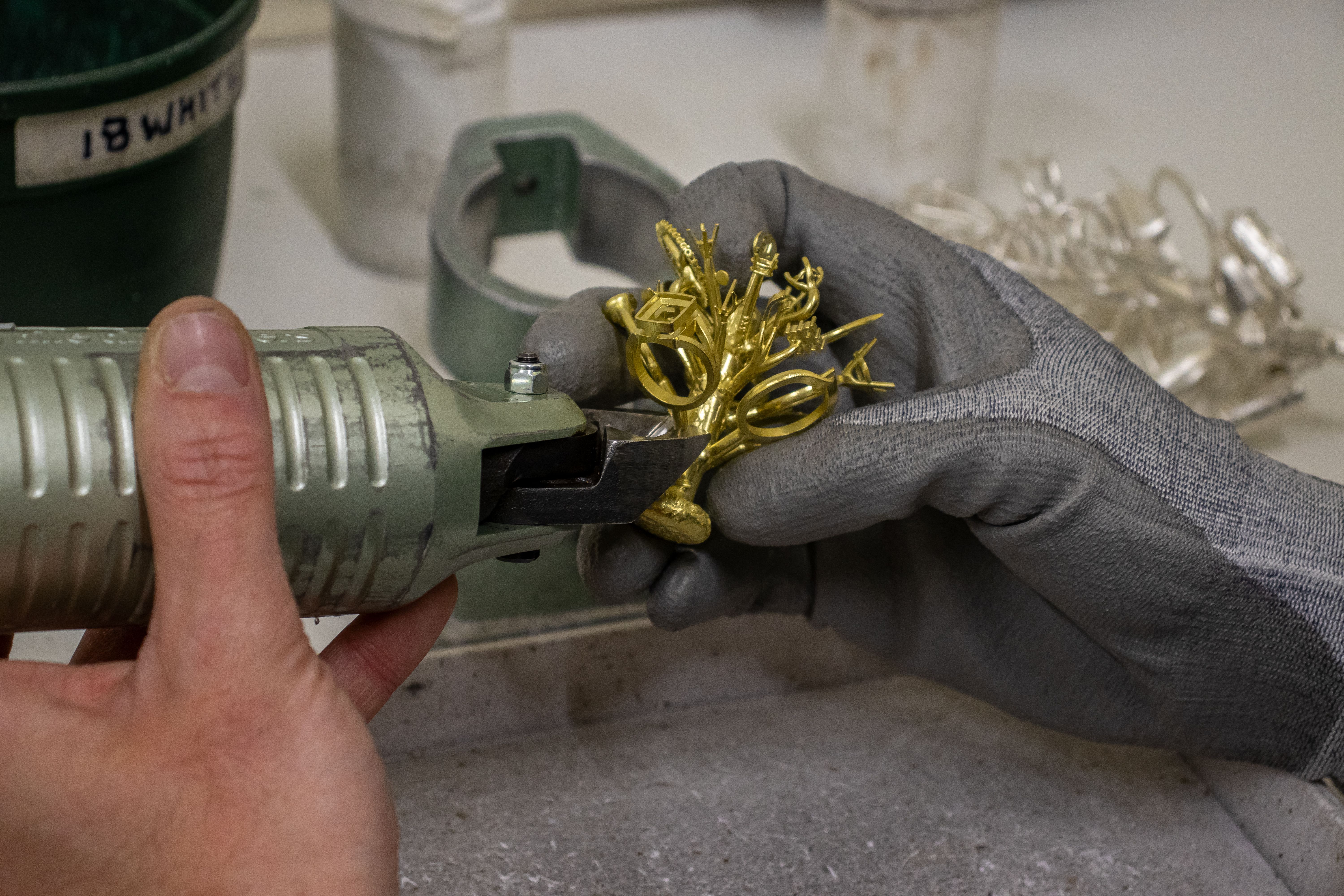 A person wearing gray gloves uses a tool to shape a golden, intricate metal piece in a workshop, conveying craftsmanship and precision.