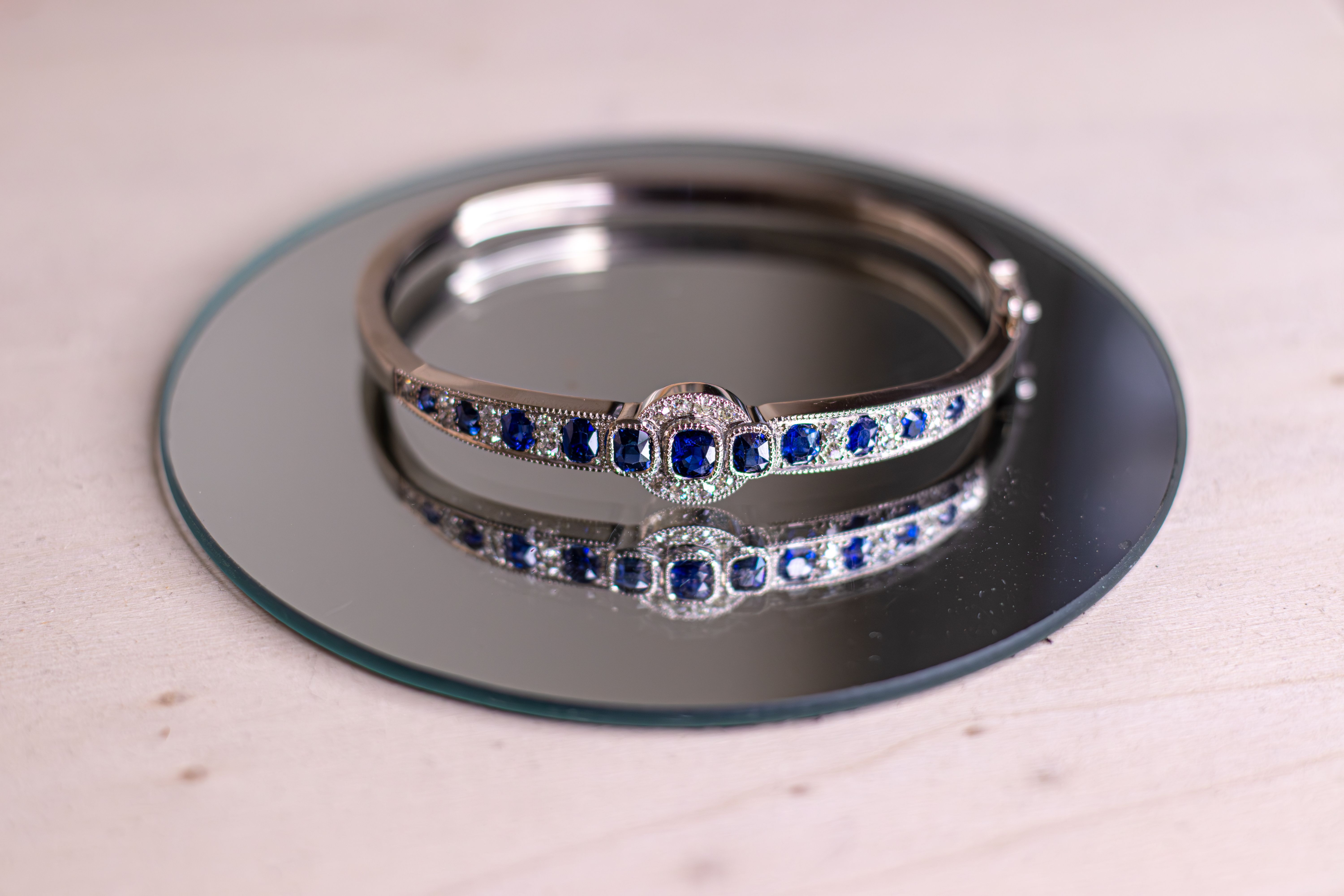 Silver bangle bracelet featuring navy blue stones and clear accent stones, resting on a round mirror.