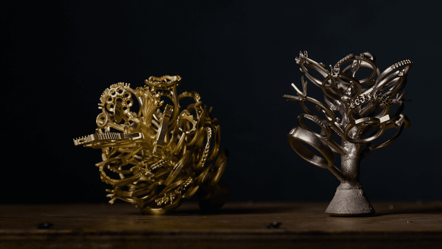 High-contrast image of two precious metal jewellery casting trees: one in polished yellow gold, and one in silver or white gold ring mounts.