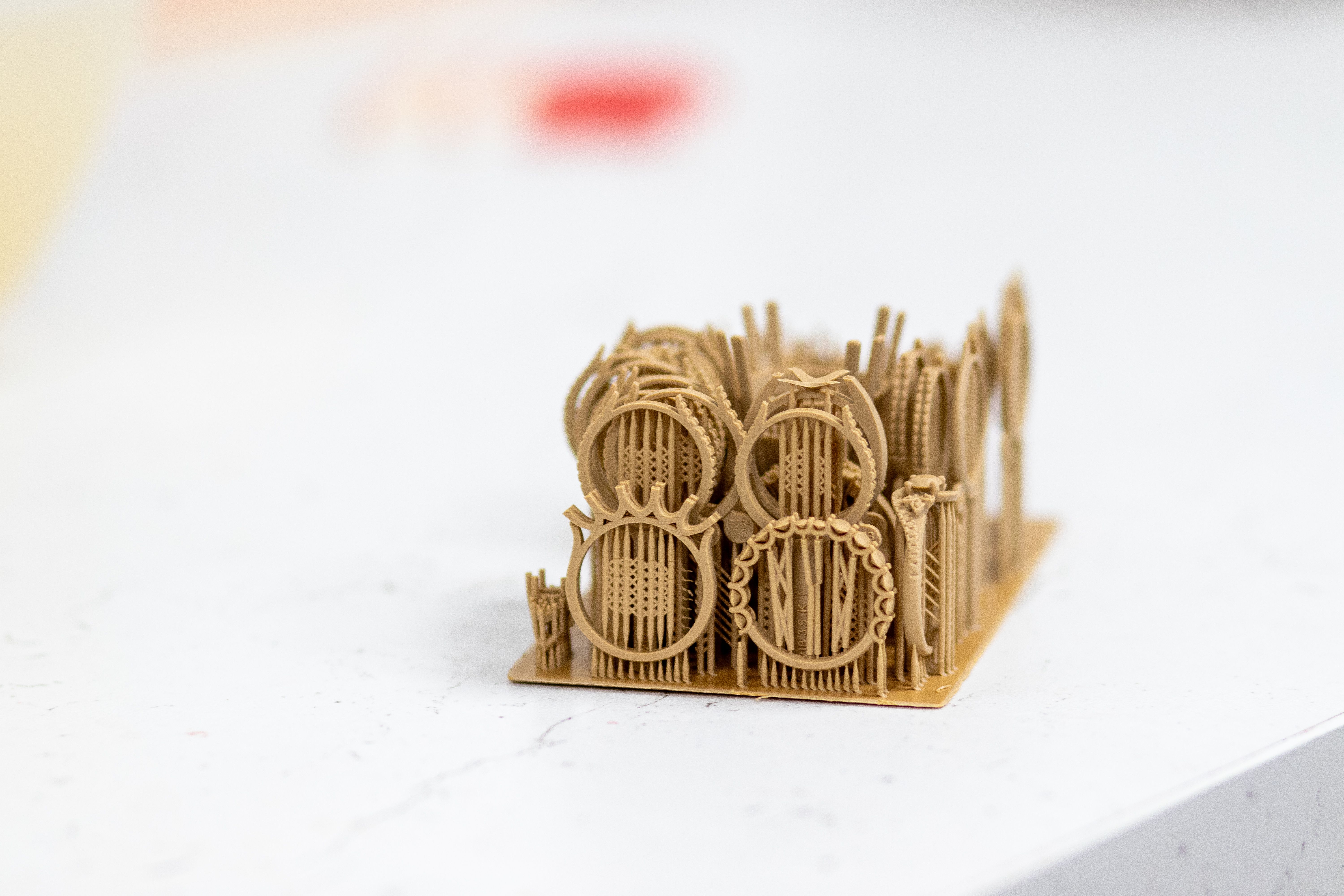 A small, intricate 3D-printed structure sits on a white surface. The design features circular and vertical elements, suggesting a complex, technical model.