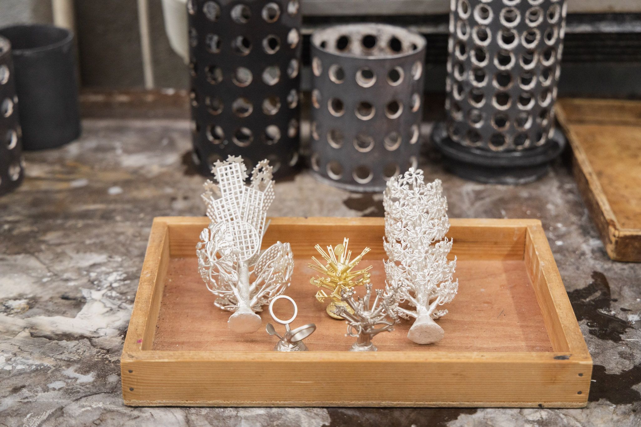 Various jewelry pieces and ring molds on a tray in a workshop, showing the lost wax casting process.