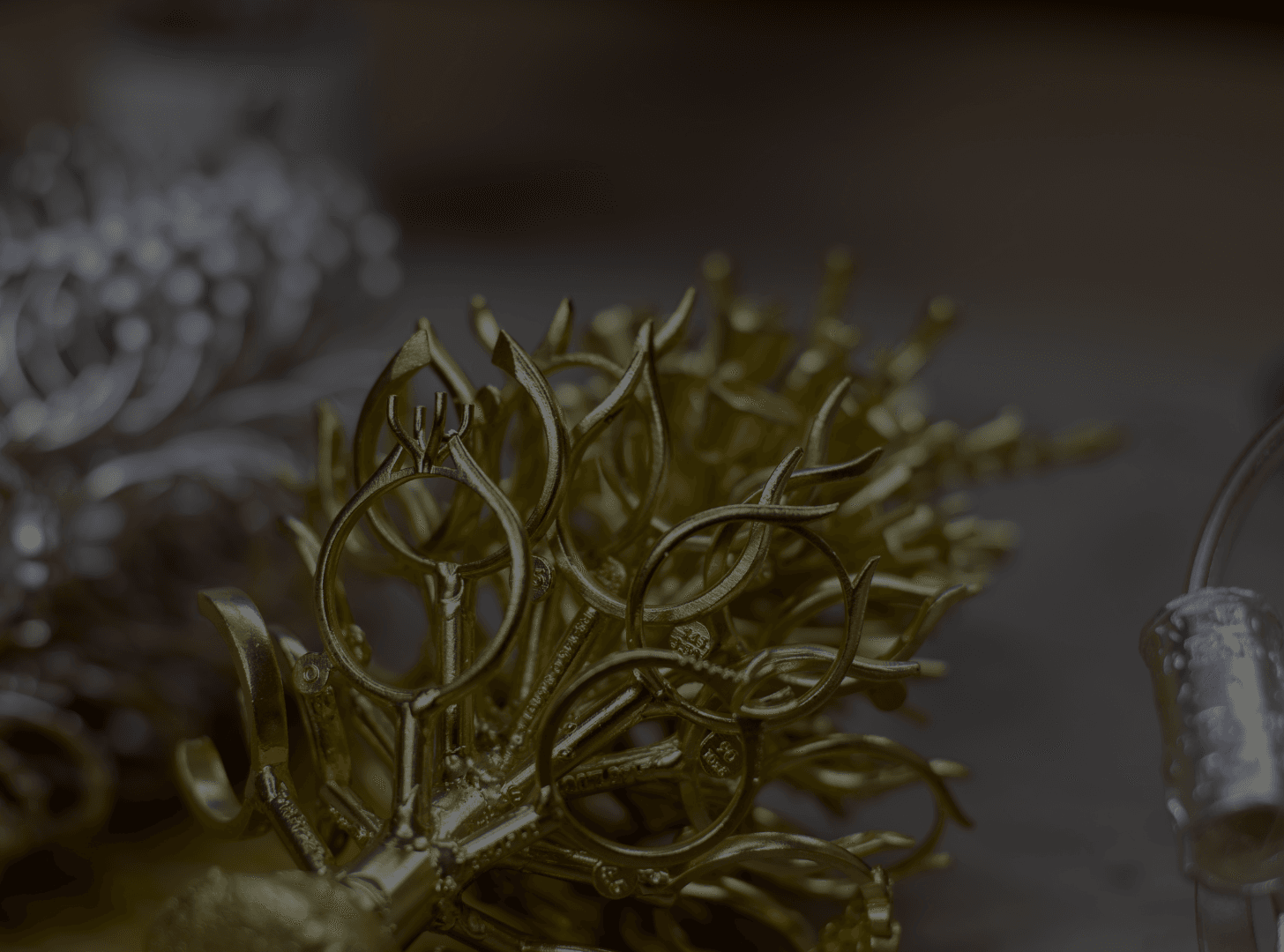 A close-up shows a cluster of intricate, unpolished gold jewelry castings, often called a "tree," with individual ring and earring components visible, alongside other metal pieces in the background.